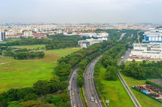 Aerial view of Singapore with car traffic on highway, green landscape with modern citysape in background