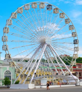 KIEV, UKRAINE - MAY 11, 2019: People walking by giant Ferries Wheel in Kiev, Ukraine. St. Andrew chuch in the background