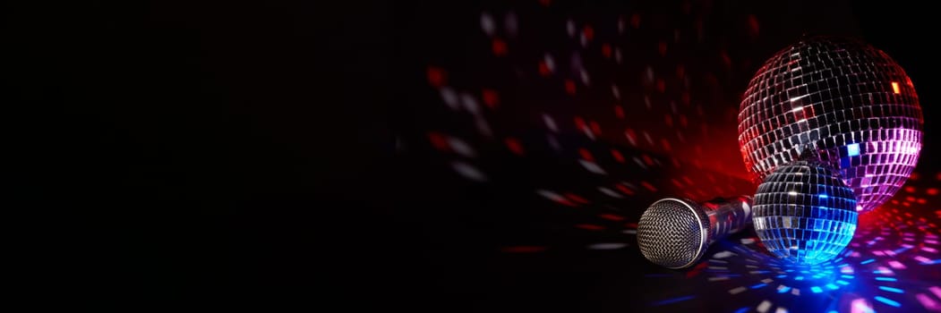 Glittering mirror disco balls and microphone on dark background with multicolor lighting. Copy space. Weekend or holiday party. Karaoke club. For advertising or web design.