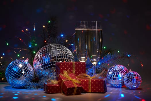 Champagne flutes, mirror balls (disco ball), fir branch, on dark background with colorful LED lights garland. New Year and Christmas. Weekend or holiday party.