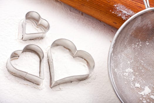Cookie cutters, flour sieve and wooden rolling pin on a floured baking mat