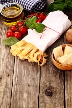 Fresh ingredients for Italian pasta standing ready to cook on a rustic wooden table with olive oil, cherry tomatoes, parmesan cheese, dried pasta and basil