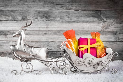 Close up Adorable Silver Reindeer and Santa Sleigh with Presents for Christmas Decoration. Displayed on Man Made Snow with Gray Wooden Wall Background.