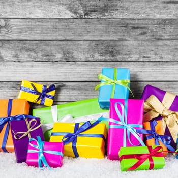 Close up Assorted Colored Christmas Gift Boxes with Ribbons on Snow with Wooden Wall Background.