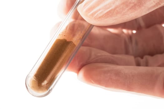Fingers holding test tube with brown chemical powder.