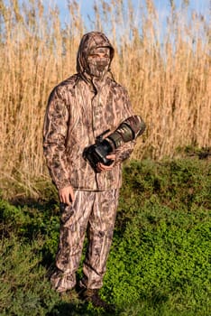 Naturalist photographer in action, with camouflage and camera, in the wilderness.