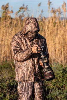 Naturalist photographer in action, with camouflage and camera, in the wilderness.