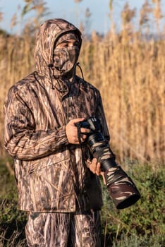 Naturalist photographer in action, with camouflage and camera, in the wilderness.