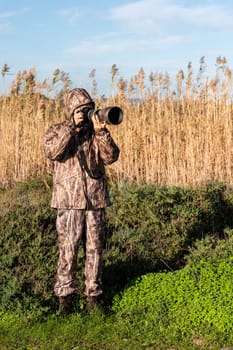 Naturalist photographer in action, with camouflage and camera, in the wilderness.