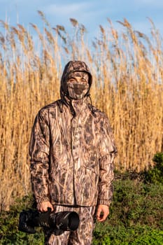 Naturalist photographer in action, with camouflage and camera, in the wilderness.