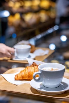 Coffee and croissant served in a tray on the counter in a blurry pastry shop background