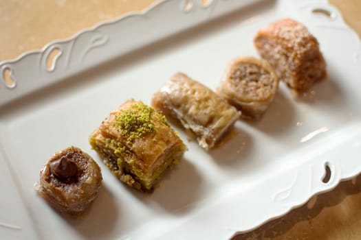 Five different mini baklava traditional turkish dessert on white plate.