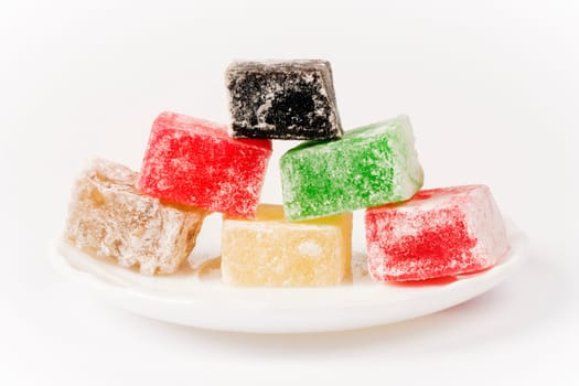 Different colorful Turkish delight cubes are on plate on white background.