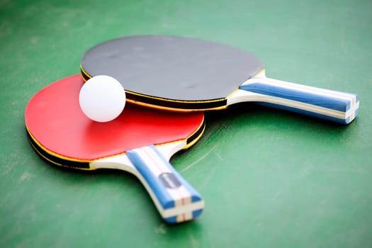 Table tennis set or pingpong set, two rackets and a ball are on green table.