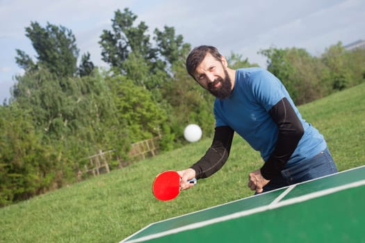 The bearded man is playing table tennis outdoors, active life concept.