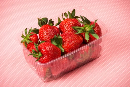 Red ripe strawberries in plastic package on pink spotted background.