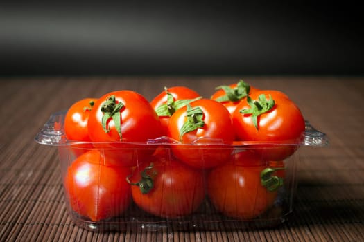 Red ripe organic tomatoes are in transparent plastic package on dark background.
