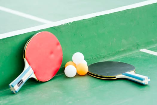 Table tennis set or pingpong set, two rackets and some balls are on green table.