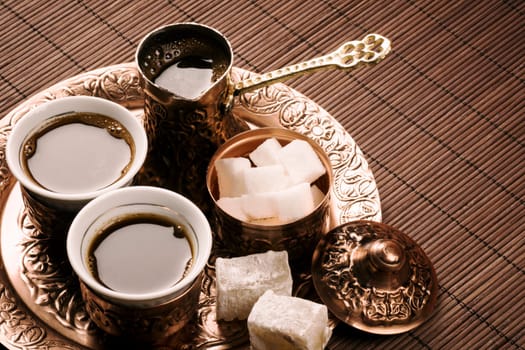 Traditional Turkish coffee set with two coffee cups, sugar and Turkish delight on brown background.