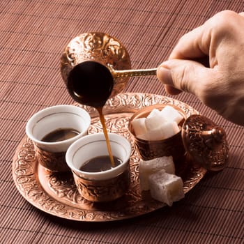 The male hand is pouring coffee in cup of coffee, copper Turkish coffee set.
