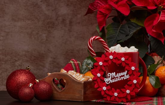 Red Poinsettia flowers, tray with ginger cookies, mandarines, mug with hot cocoa and marshmallows. fir ornaments, gifts on brown background with copy space. Winter holidays. New Year, Christmas treat