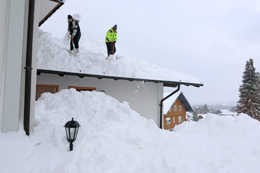 Two men shoveling high heavy snow from a house roof