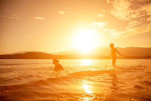 pair of children playing in the sea, shot taken at sunset, hills in the background. Corsica.