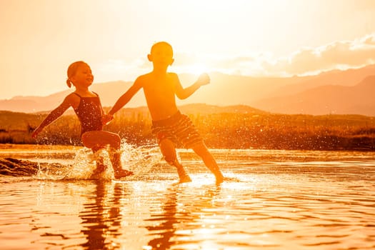 portrait of two children aged 3 and 6 playing in the sea and spraying water around them. Backlight image at sunset