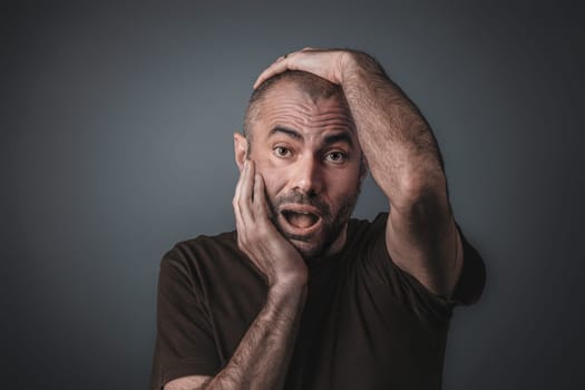 Portrait of a man holding his head with both hands with a surprised expression.