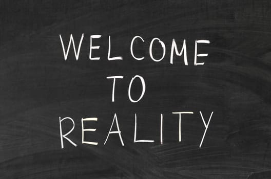 Welcome to reality phrase handwritten on the school blackboard