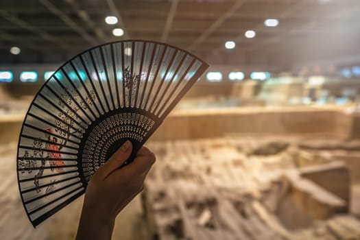 Woman holding chinese fan spread out inside the building in Terracota Warriors Museum, Xian town, China