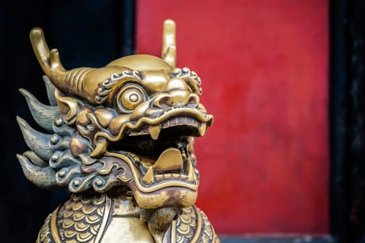 Statue of mystical Chinese golden brass guardian lion on red wall background in the courtyard of the Buddhist Wenshu Temple Monastery, Chengdu, Sichuan Province, China