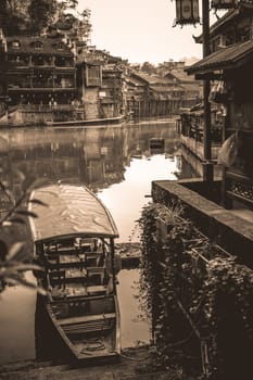 Old historic wooden tourist boat on the riverbanks of Tuo river, flowing through the centre of Fenghuang Old Town, China