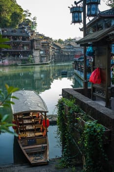 Old historic wooden tourist boat on the riverbanks of Tuo river, flowing through the centre of Fenghuang Old Town, China
