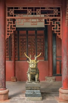 Statue of mystical Chinese golden brass guardian lion on red wall background in the courtyard of the Buddhist Wenshu Temple Monastery, Chengdu, Sichuan Province, China