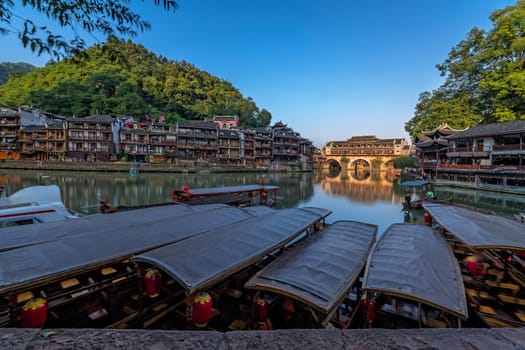 Old historic wooden tourist boats on the riverbanks of Tuo river, flowing through the centre of Feng huang Old Town, China