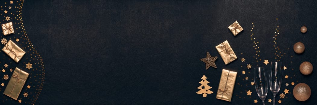 Golden Christmas decorations, gift boxes, champagne flutes on black background. Top view, copy space. Design element for greeting card, invitation, advertising. Extra wide panorama banner background