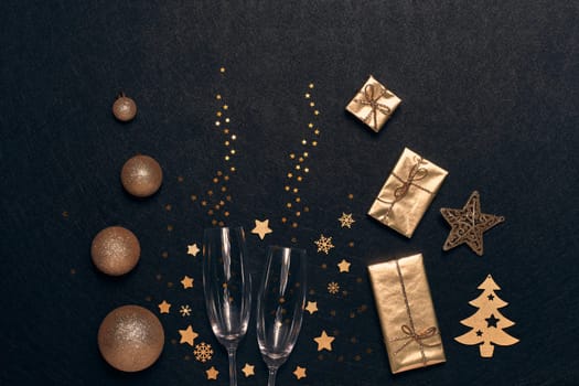 Festive composition with golden Christmas decorations, gift boxes, empty champagne flutes on black background. Top view. Design element for greeting card, invitation, advertising