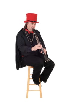 A middle age indigenous man playing his clarinet in a black outfit and.red hat and bow, isolated for white background.