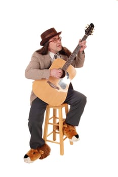A middle age indigenous man in fancy shoes sitting and playing.his guitar in a jacket and hat, isolated for white background.