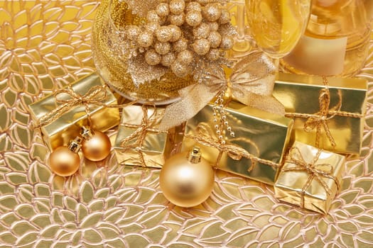 Golden Christmas ornaments, gift boxes, champagne bottle and full champagne flutes on gold background. Christmas. New Year. Design element for greeting card, invitation, advertising