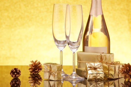 Golden gift boxes and fir cones, champagne bottle and empty champagne flutes on festive gold background. Christmas. New Year.  Design element for greeting card, invitation, advertising