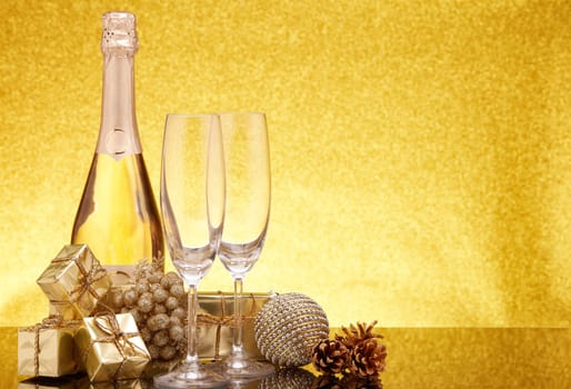 Golden Christmas ornaments, gift boxes, champagne bottle and empty champagne flutes on gold background with copy space. Christmas. New Year. Design element for greeting card, invitation, advertising