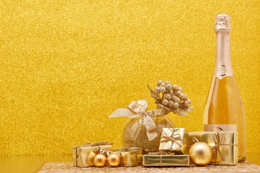 Golden Christmas ornaments, gift boxes and champagne bottle on gold background with copy space. Christmas. New Year. Design element for greeting card, invitation, advertising