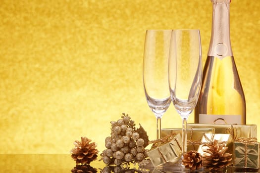 Golden Christmas ornaments, gift boxes, champagne bottle and empty champagne flutes on gold background with copy space. Christmas. New Year. Design element for greeting card, invitation, advertising