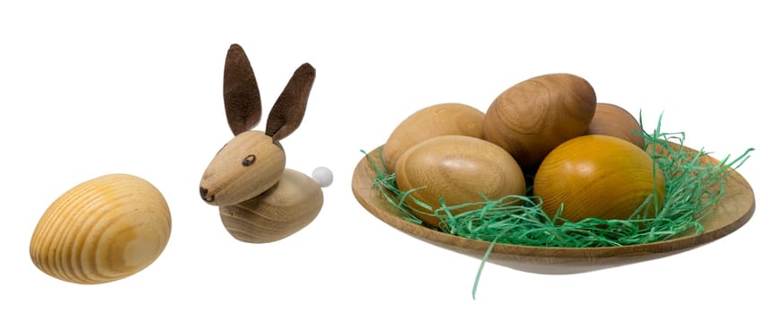 Hand-turned wooden eggs in a small wooden bowl with toy Easter bunnies isolated on white
