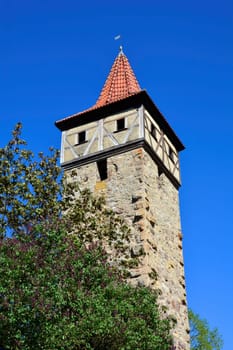 Old square tower with red roof, tree in front, with blue sky, in Ostheim vor der Rhön, Germany