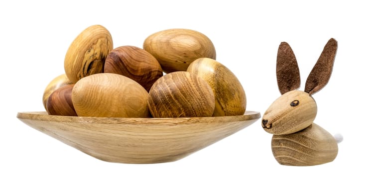 Hand-turned wooden eggs in a small wooden bowl with toy Easter bunnies isolated on white