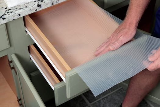 Adult white man inserting a clear thick plastic drawer liner with lines in it into a bathroom drawer. Closeup of adult guy lining a green wood and white bathroom drawers with plastic protection.