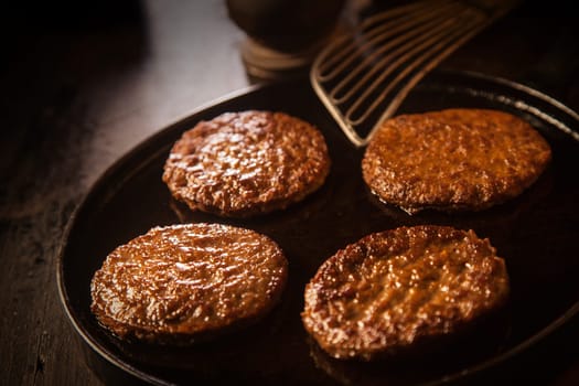 Four round beef burger patties or frikadeller pan fried in an old metal frying pan standing ready for use in preparing hamburgers